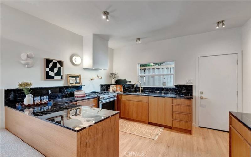 Kitchen area with marble countertops, custom minimalist vertical wood-grain cabinets and new stainless appliances