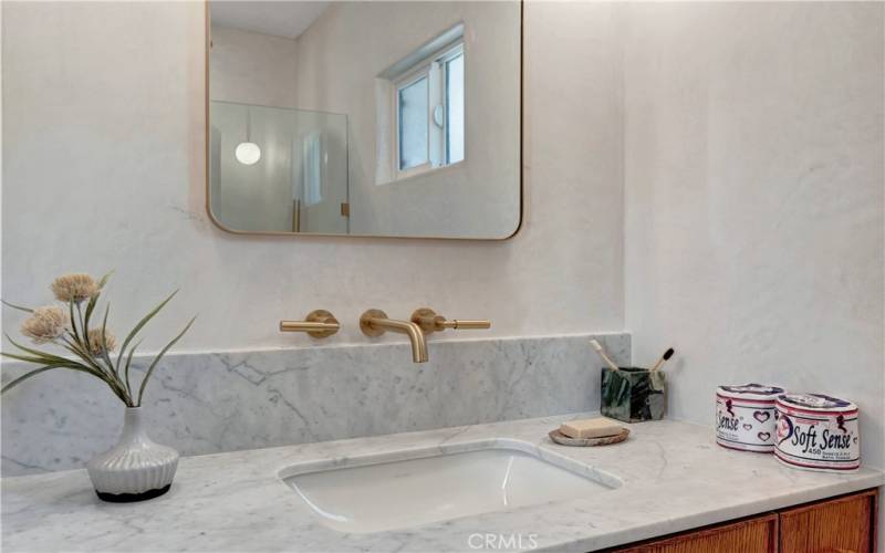 Primary bathroom with marble counter, and wall-mounted brass faucets