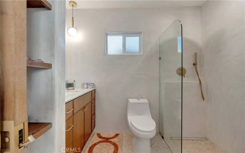 Primary bathroom is wet room with floor to ceiling stucco walls with marble counters, durable hexagonal terrazzo floors, custom shelving, frameless glass wet room, and dual rainshower and handheld shower