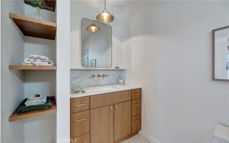 Bathroom 2 with marble counters, wall-mounted faucets, and custom shelving