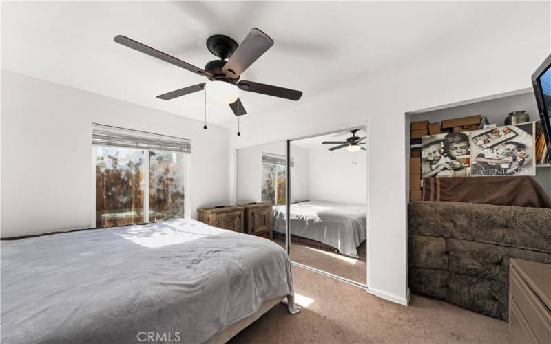 Guest bedroom with a large window, blinds, ceiling fan with a light and closet with mirrored doors.