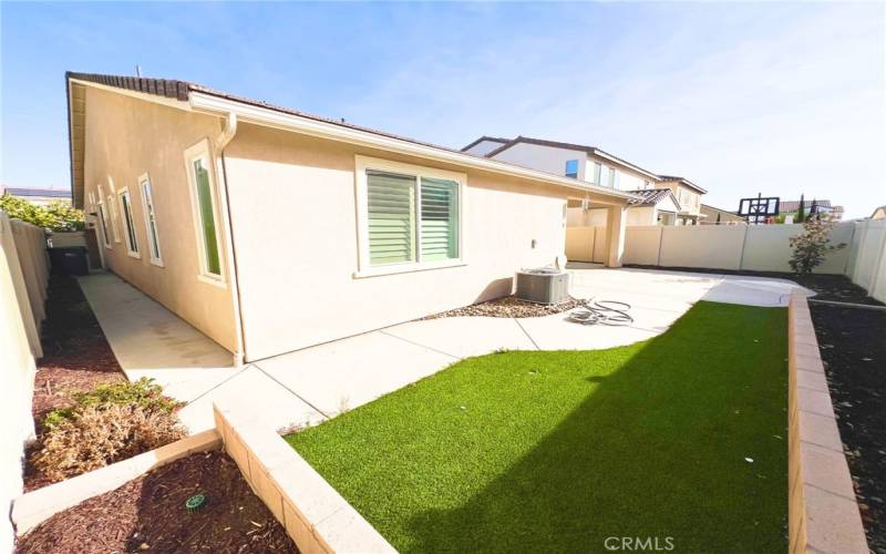 Beautifully landscaped backyard with artificial grass, flower beds, a patio, and concrete surrounding the home