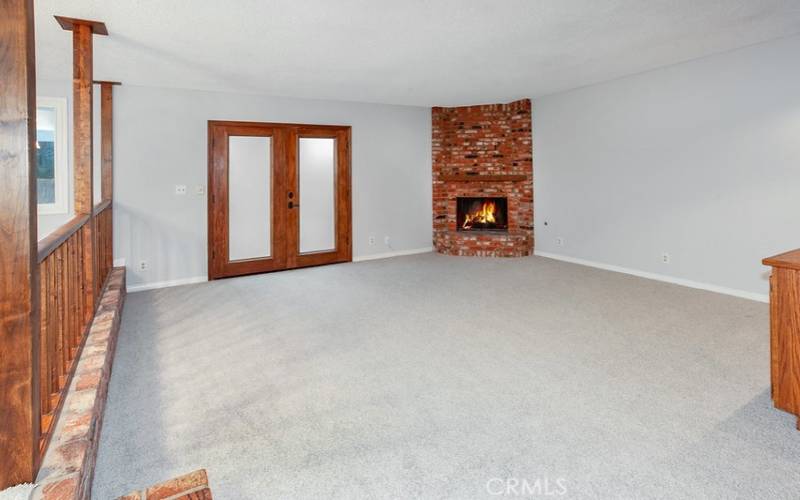 Separate expansive step-down family room with floor-to-ceiling raised hearth brick fireplace, custom-built wood bookcase with storage, wood-framed French doors that lead to the backyard patio and plush new carpet.