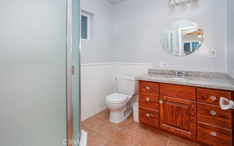 Primary en suite bathroom with vanity, undermount basin, wainscoting, glass-enclosed step-in shower, and tile floors.