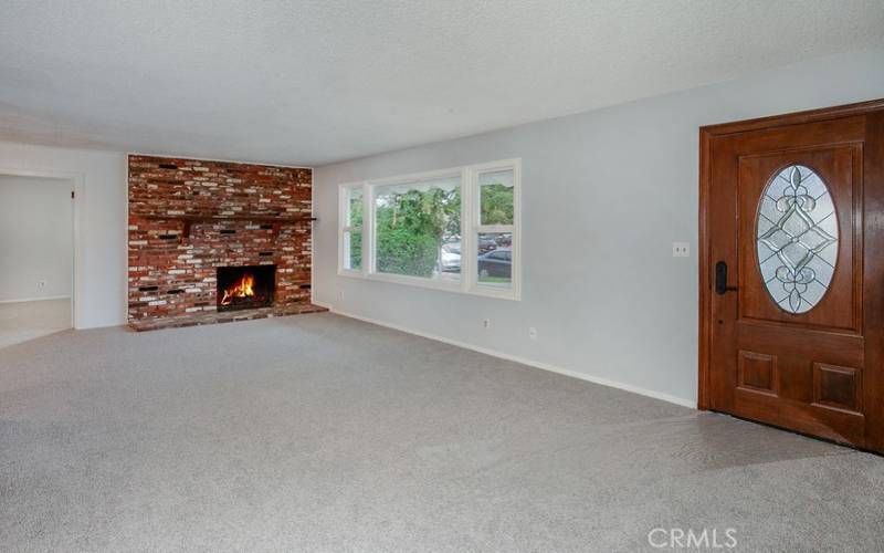 The living room is drenched in natural light from a multitude of windows and is enhanced by a floor-to-ceiling brick fireplace with mantle, and plush new wall-to-wall carpet.