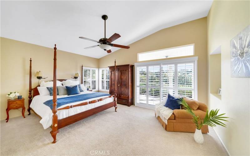 Primary bedroom with vaulted ceiling, wood shutter, sliding door access to back patio