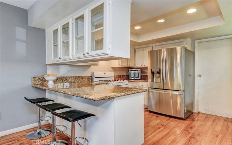 Beautiful kitchen with granite counters, recessed lights and glass-door cabinets above peninsula