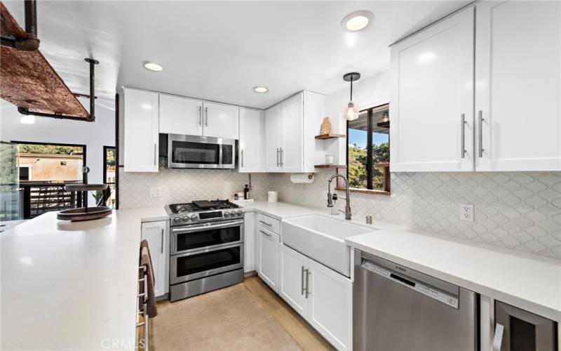 Remodeled kitchen includes new cabinets, tile backsplash, stainless steel appliances, and large farmhouse sink