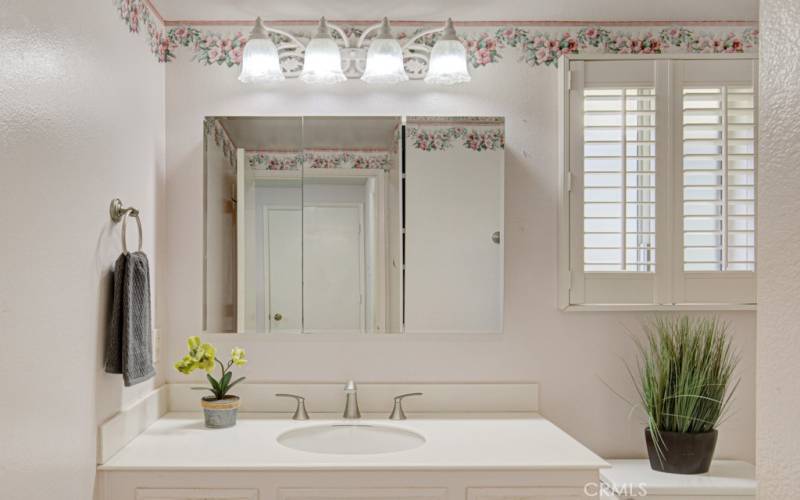 Pretty primary bathroom has a nice vanity and triple mirror medicine cabinet.  Shutters on the window are just the perfect touch.