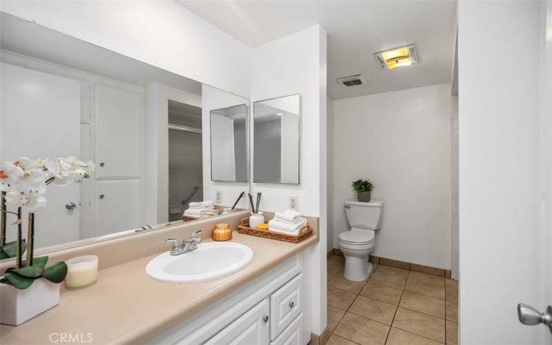 Primary bathroom has long countertop with drawers underneath, cabinets and water heater opposite the sink, bathtub with shower is opposite the the toilet.