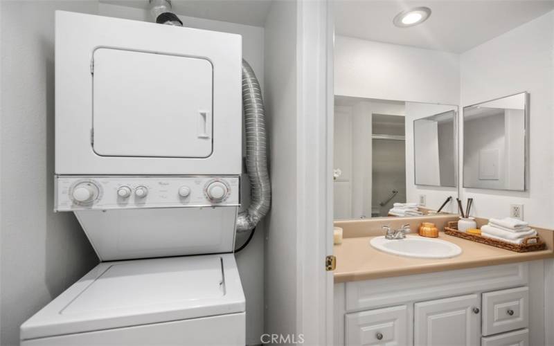 Stacked laundry machine included, is located in hallway outside of bathroom.