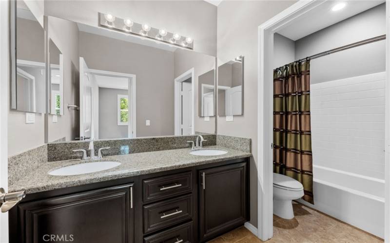 The secondary bathroom features dual medicine cabinets, tile flooring and a granite vanity countertop.