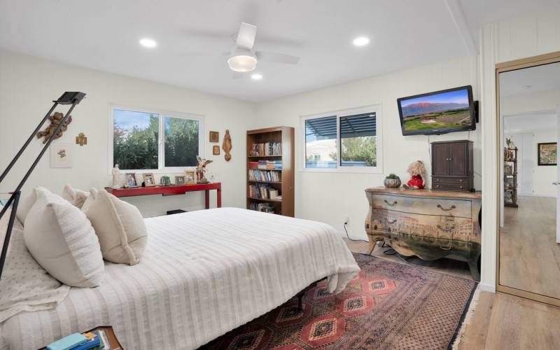 Primary bedroom with 2 large windows, recessed lighting, ceiling fan and tv mounted on the wall