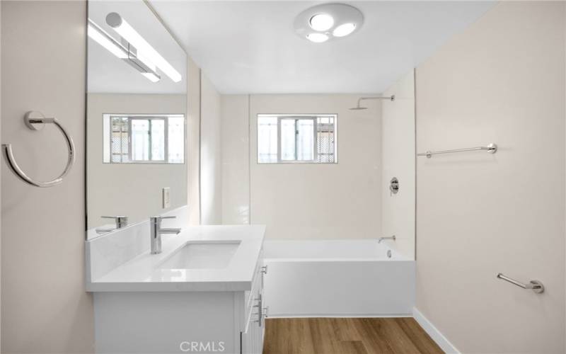 This bathroom has been completely remodeled with a new sink, flooring, lighting, and finishes. The large tub has a high shower head for a modern feel. The subway-style panels are easy to clean. A hidden bench behind the sink provides a place to relax in the privacy of your own home.