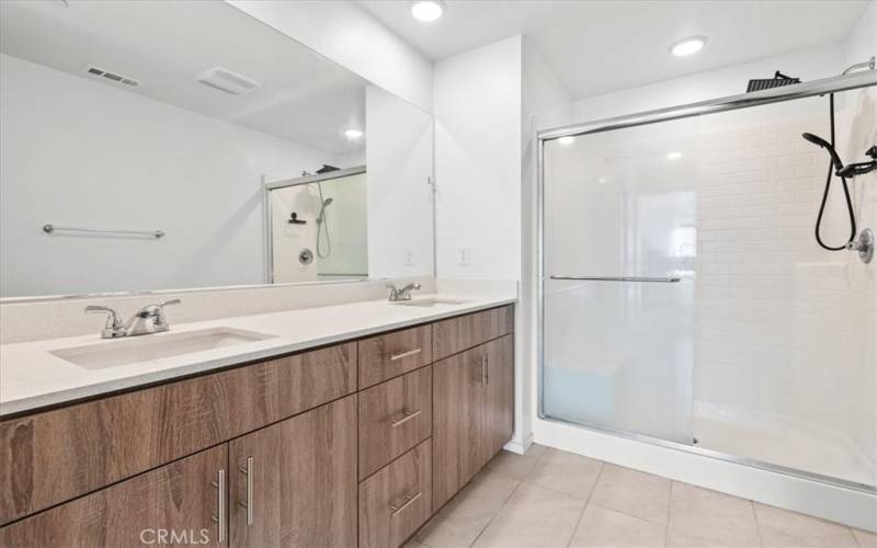  A connected en-suite bathroom with dual sinks, a walk-in shower, and elegant finishes.