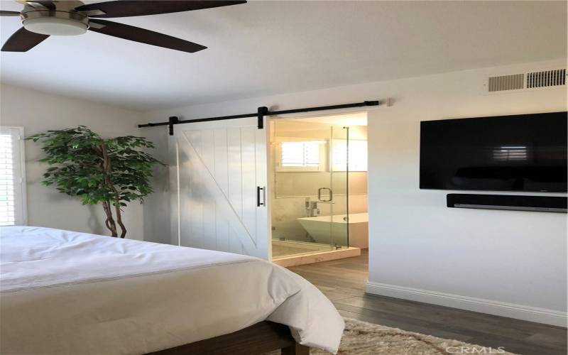 Master bedroom with Barn door open to custom shower, bath and walk in closet with built-ins.