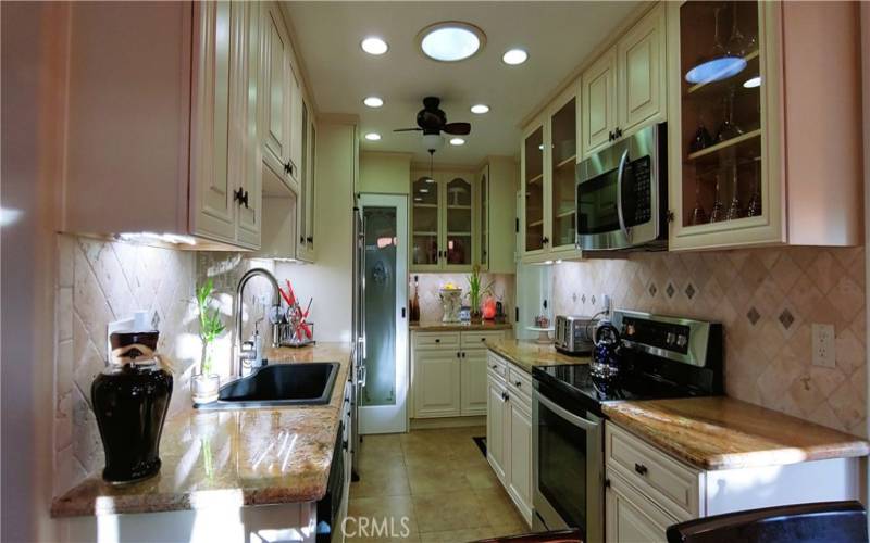 Kitchen with granite countertops,custom cabinets, black granite sink,stainless steel appliances, tumbled marble backsplash w/glass inserts, imported porcelain tiles .Pantry  in background.