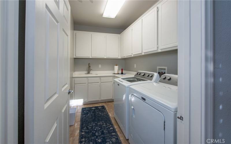 Big laundry room with cabinets galore, tile floors and sink.