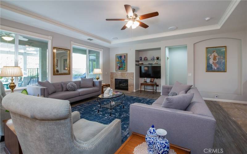 The living room has wood type laminate floors, a tile fireplace, entertainment niche, coffered ceiling and ceiling fan.