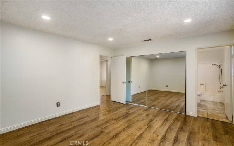 Ample sized primary bedroom with mirrored closet doors and adjoining bathroom.