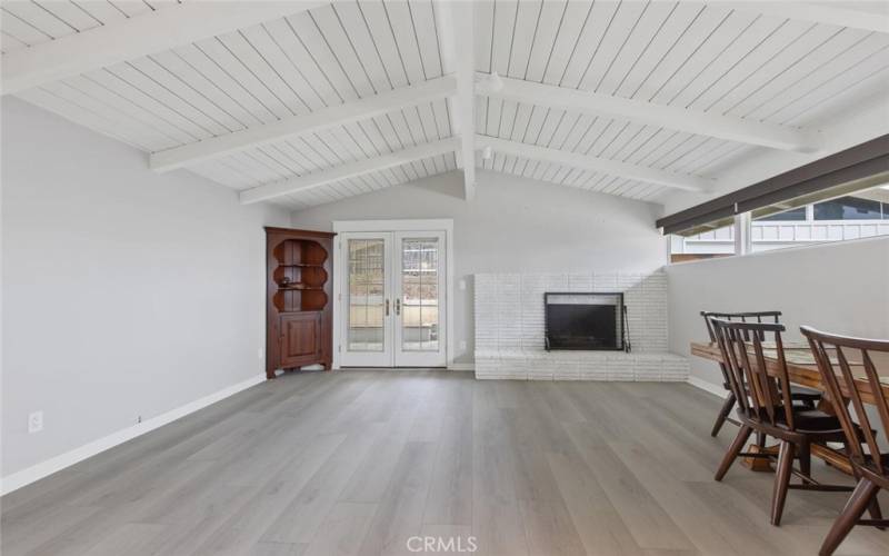 Family Room with painted open beam ceiling gives open feeling, Windows stretch along the right wall (south), allowing natural light, but also have pull-down shades. The French Pella doors open onto a covered concrete Patio and fenced Back Yard.