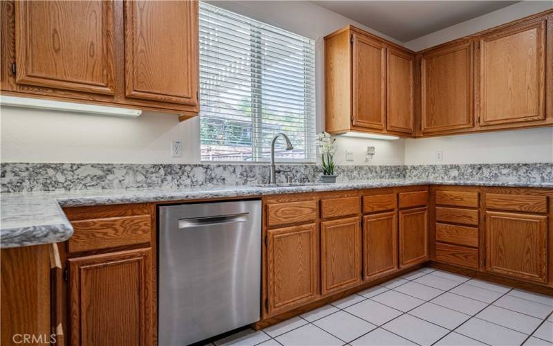 New quartz grey/white countertops with new stainless steel appliances and new stainless steel farm sink. Oak cupboards, and dishwaher in the photo. Window above the sink overlooks the back yard patio area.