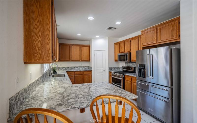 New quartz countertops and new stainless steel appliances. Kitchenaide refrigerator. Double oven with gas range and microwave above. Tons of oak cupboards. White door opens to your pantry. Recessed lighting above. Tiled flooring below.