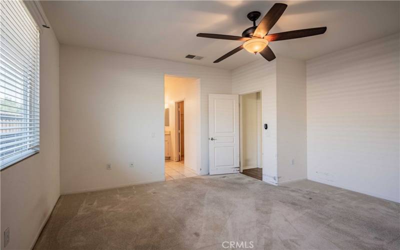 Primary bedroom with ceiling fan and carpet. En-suite bathroom and door to the right leads to the walk-in closet. Tiled bathroom with dual sinks, and privacy toilet room. Tiled  flooring in the bathroom. Carpet in the bedroom.