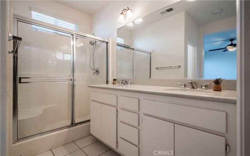 Primary en-suite bathroom with dual sinks that have quartz countertops with 2 sinks that feature stainless steel fixtures. Walk-in shower. Tiled flooring. Walk-in closet is also off of this en-suite bathroom.