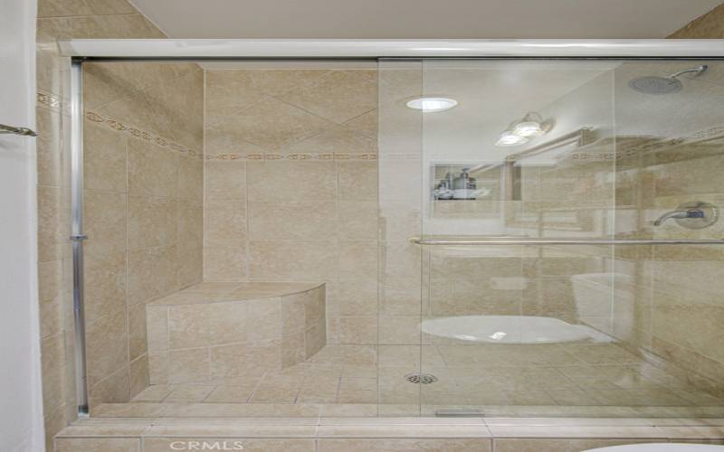 Shower in primary bathroom has a seat and convenient accessory shelf.