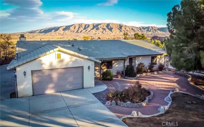 Front of the home showing the stunning views surrounding the house, huge parking area, RV parking with shed as well as the tile roof, paver stones, mature landscaping and covered porch.