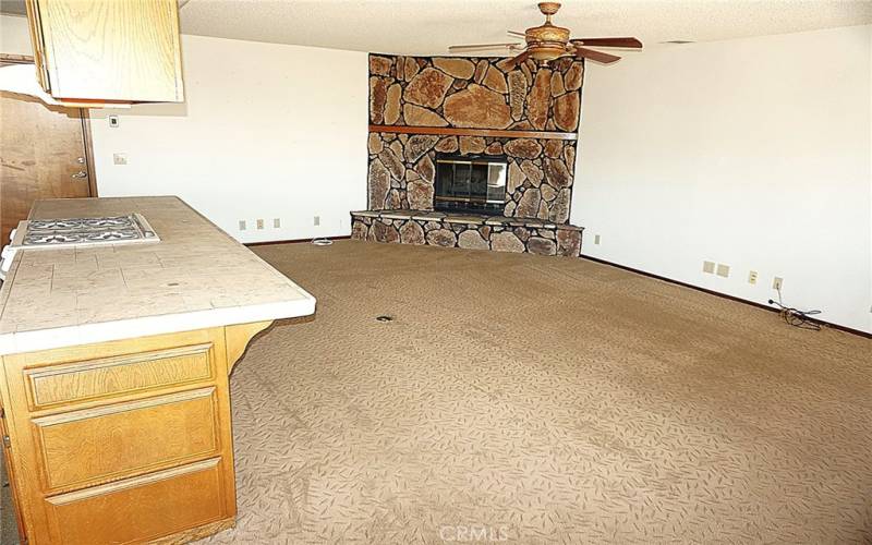 The kitchen with island is adjacent to the living room with stone faced fireplace and ceiling fan.