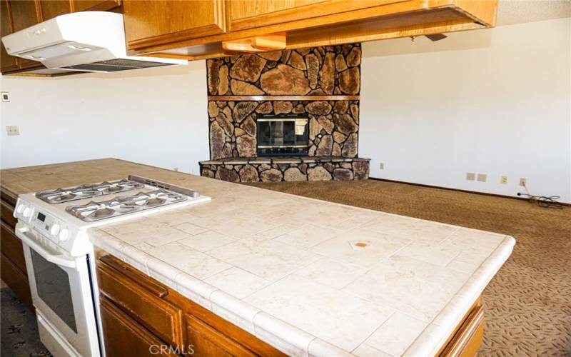 The kitchen with island is adjacent to the living room with stone faced fireplace and ceiling fan.