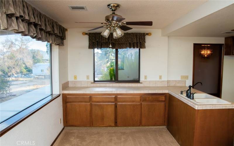 The kitchen with island is adjacent to the living room with stone faced fireplace and ceiling fan.