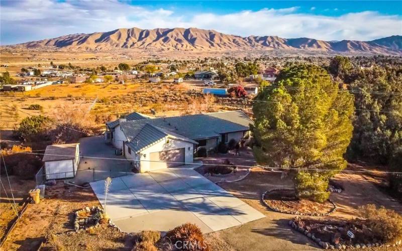 Front of the home showing the stunning views surrounding the house, huge parking area, RV parking with shed as well as the tile roof, paver stones, mature landscaping and covered porch.