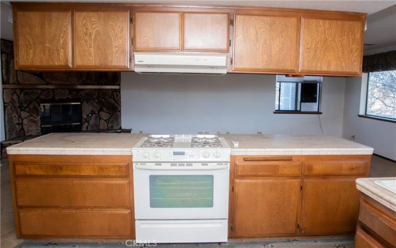 The kitchen with island is adjacent to the living room with stone faced fireplace.  Kitchen also includes tile counters, gas range, dishwasher, dining area, island, breakfast bar and stunning views of the mountains.