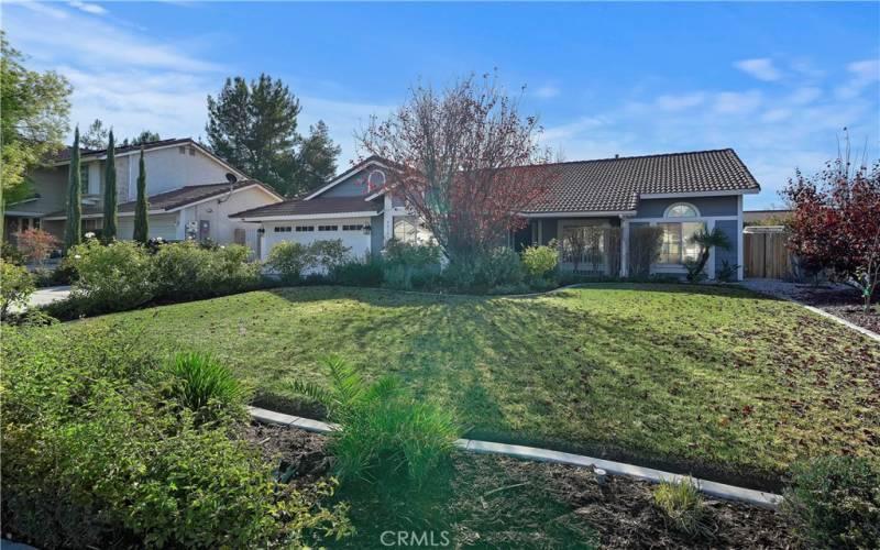 front yard with a lush lawn, shrubs, and a mature tree. The landscaped flower beds