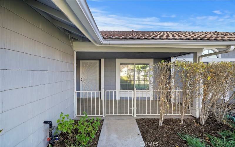 Covered front entry with a gated patio area, a security screen door, and a large front window overlooking the yard.