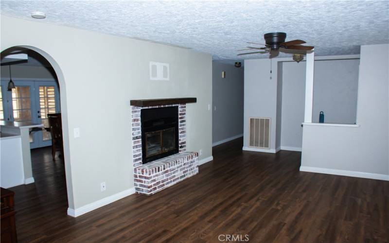 Large living room with laminate flooring, ceiling fan, 2 inch faux wood blinds, and a brick faced fireplace.