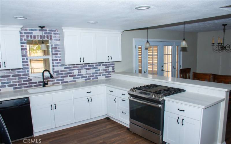 Kitchen with Quartz counters, modern white cabinets, custom backsplash, breakfast bar and stainless/black appliances.