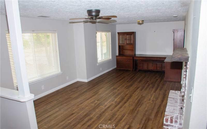 Large living room with laminate flooring, ceiling fan, 2 inch faux wood blinds, and a brick faced fireplace.