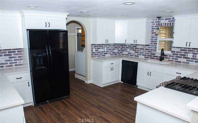 Kitchen with Quartz counters, modern white cabinets, custom backsplash, breakfast bar and stainless/black appliances.