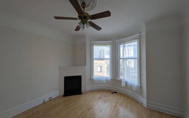 Living room w/ ceiling fan and fire place. Wide window with the view of the street and Coit Tower.