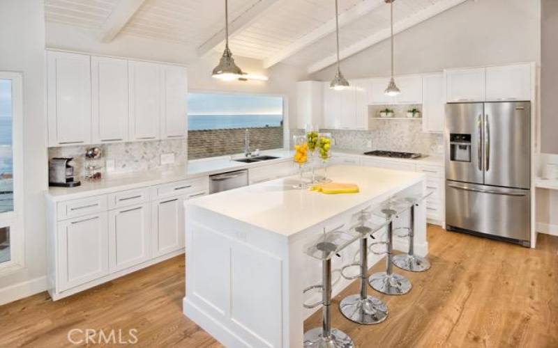 Top of the line kitchen with stainless steel appliances, kitchen island with bar, and white water ocean views.